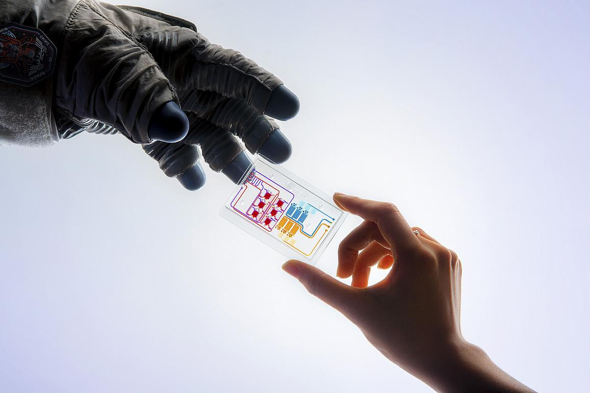 An astronaut's handing and another person's hand handing off a microchip.