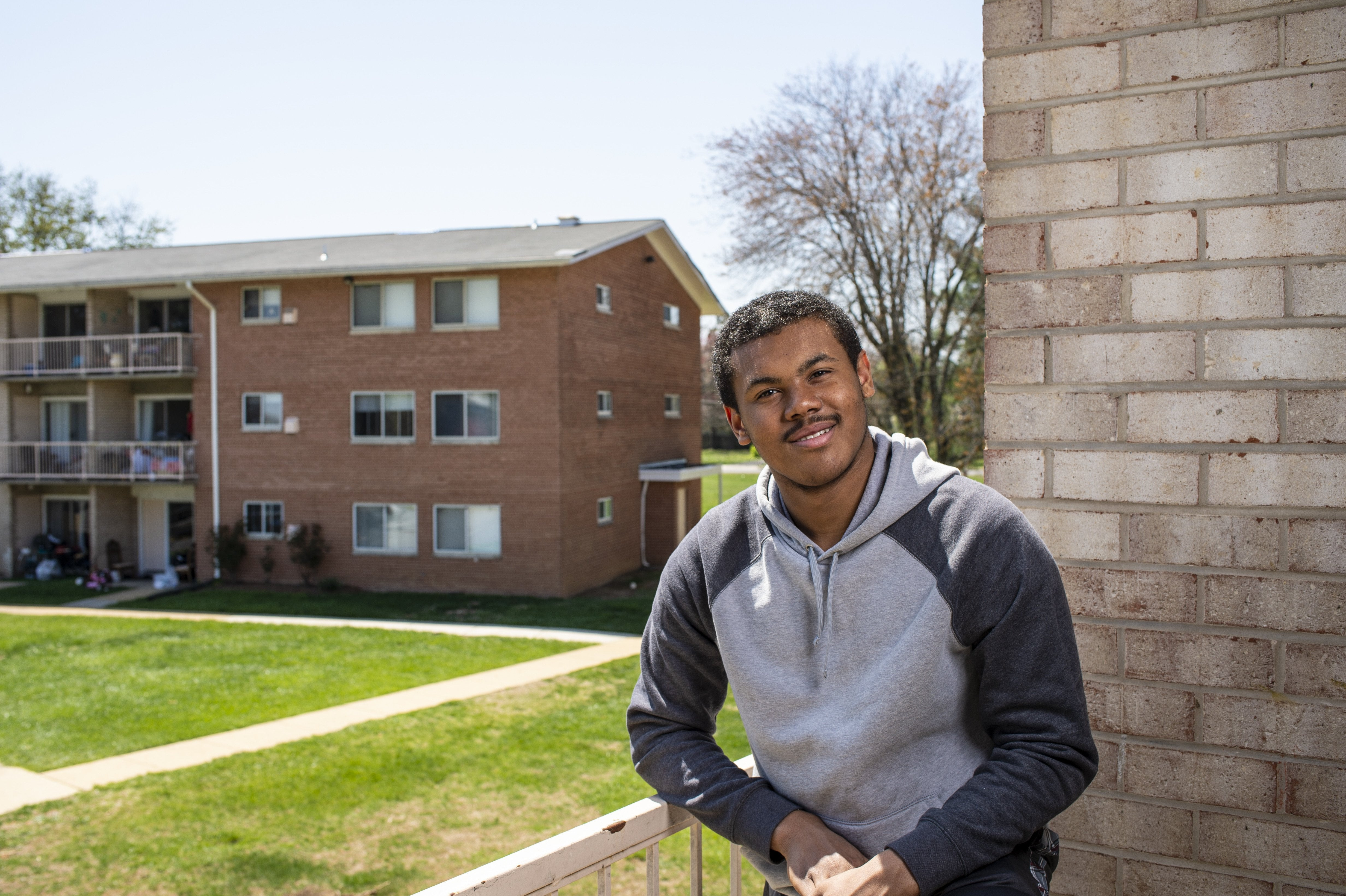A man poses for a photo on a balcony in front of a brick wall.