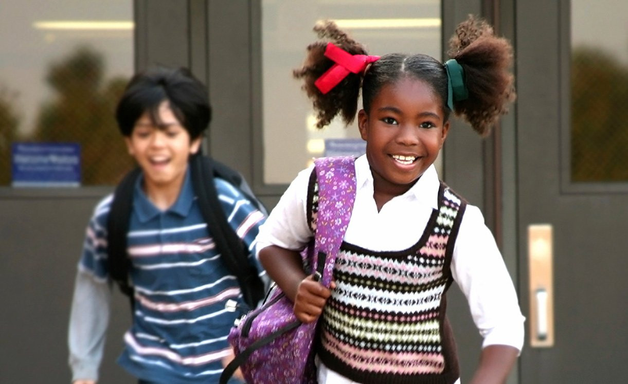 Two kids with their backpacks on leaving a school.