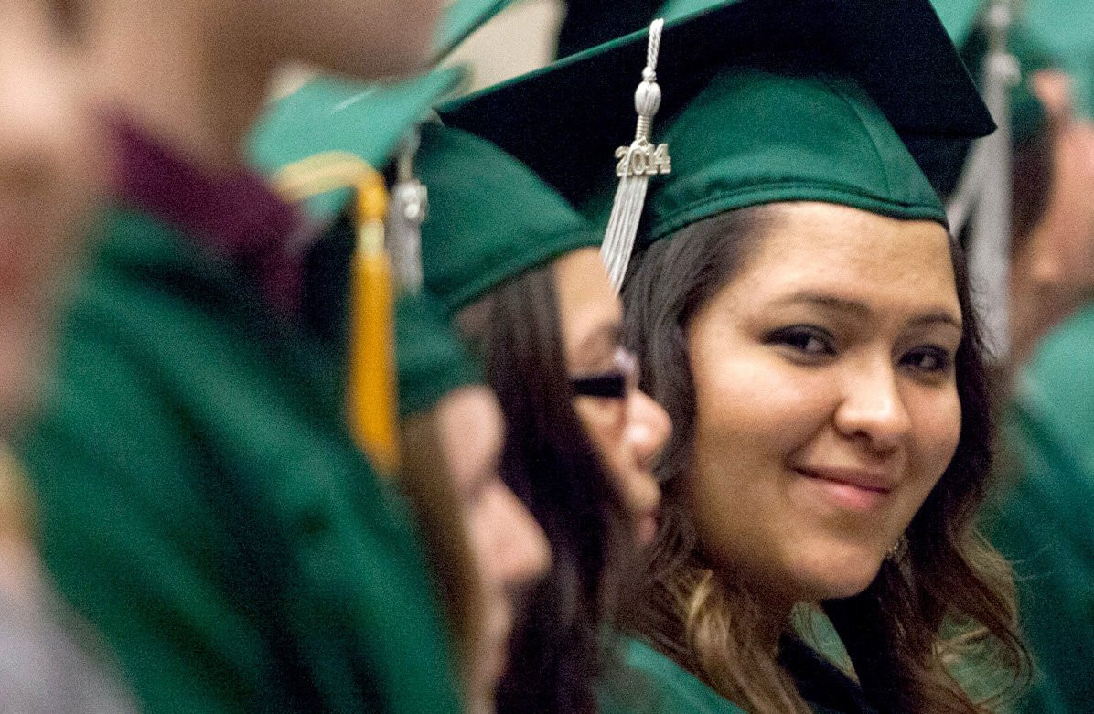 A young woman looking at the camera wearing a cap in gown standing at her graduation.