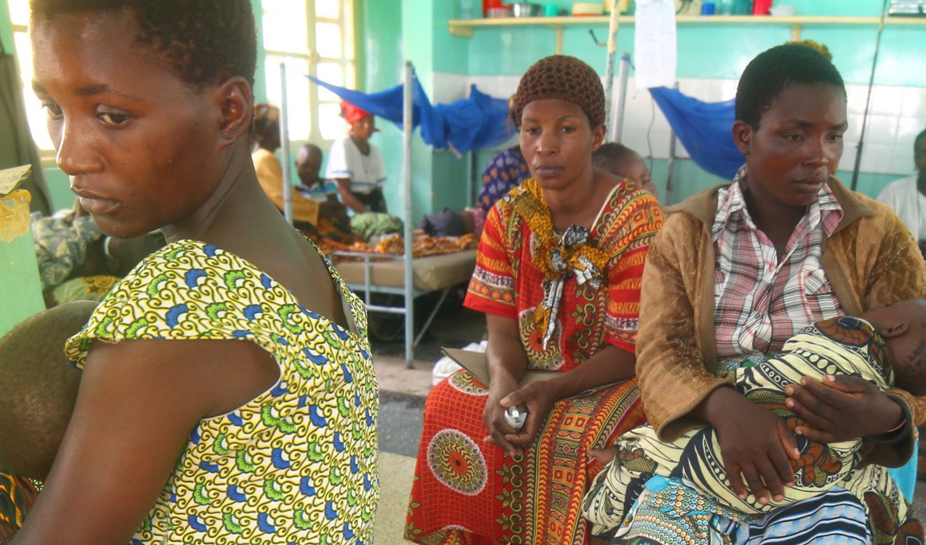 Three woman sitting in a clinic, two are holding children.
