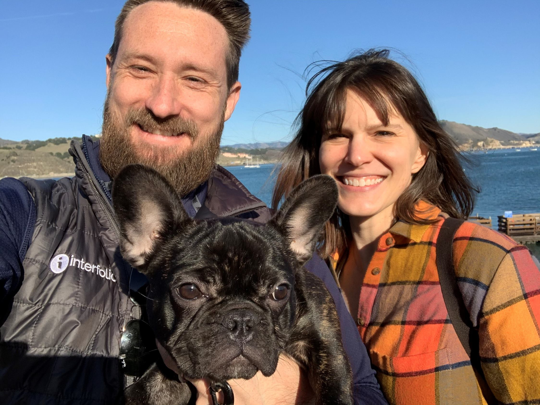 A man and a woman looking at the camera while the man is holding a black dog.