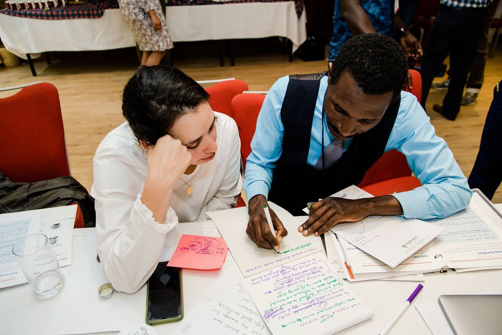 Two people work together writing something on a notepad.