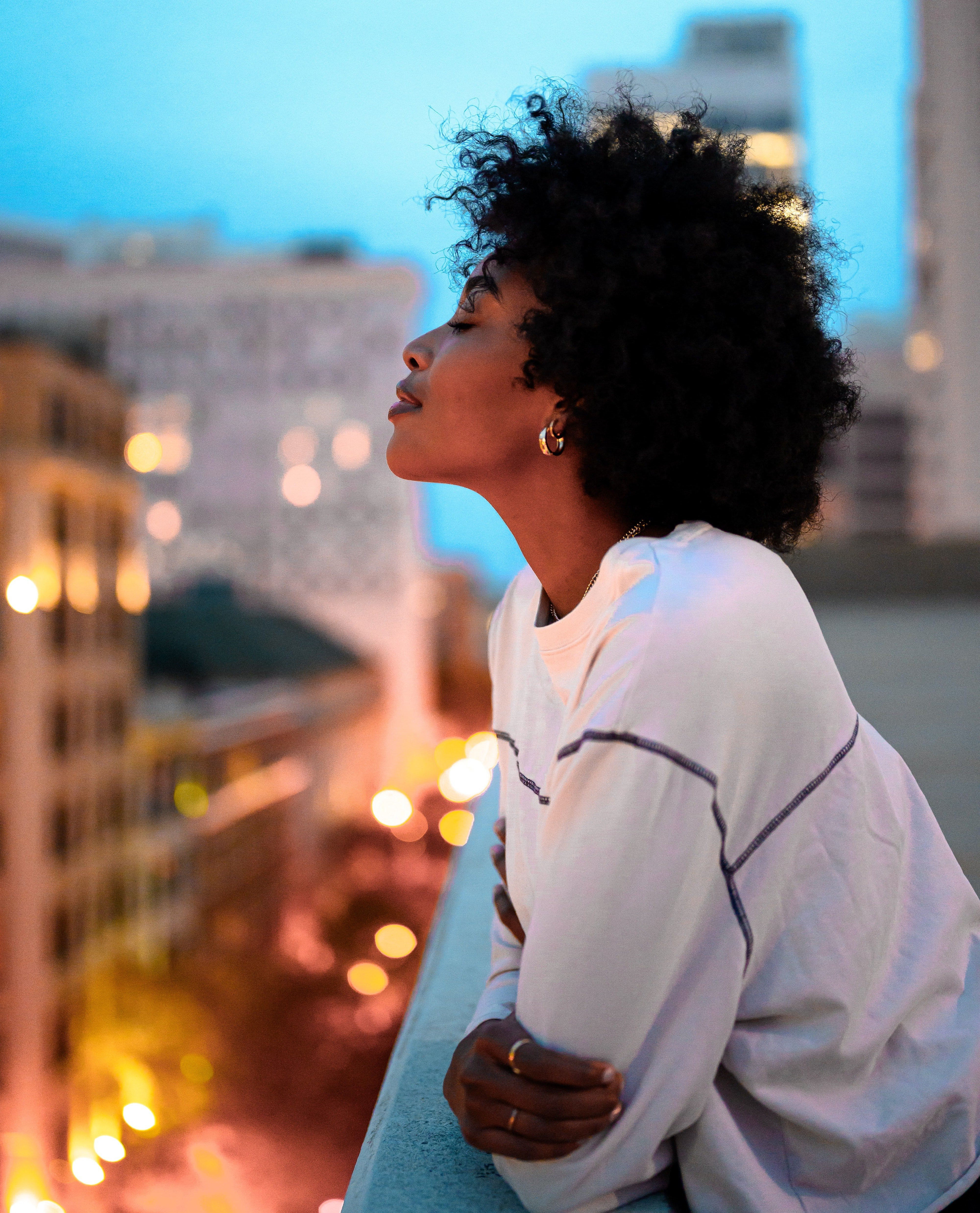 A Black woman relaxing with her eyes closed as she leans over rooftop ledge.