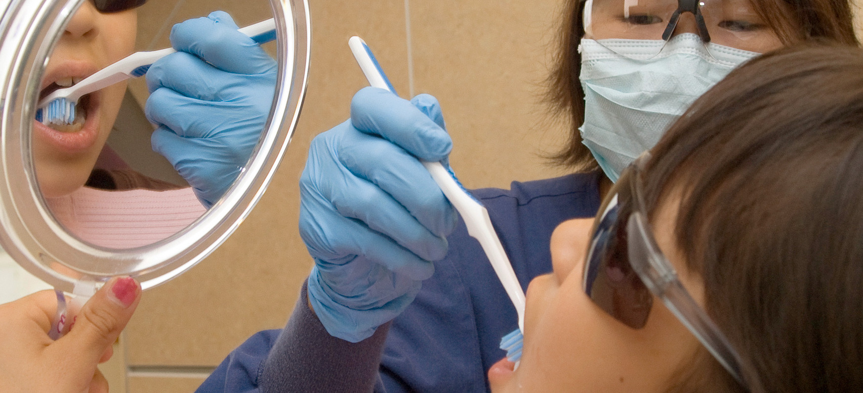 A dental therapist helping a kid brush their teeth.