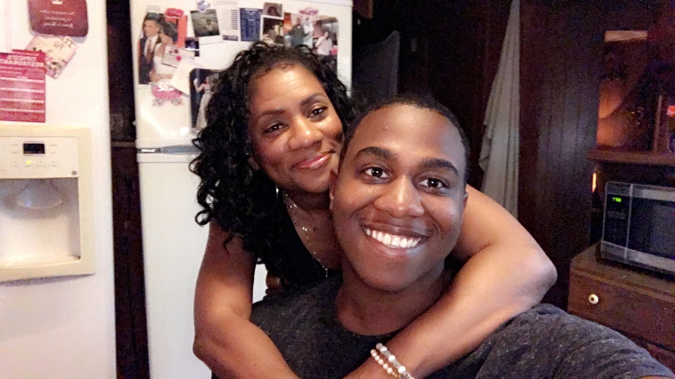 A smiling Black woman  hugging a smiling Black man in a kitchen area.