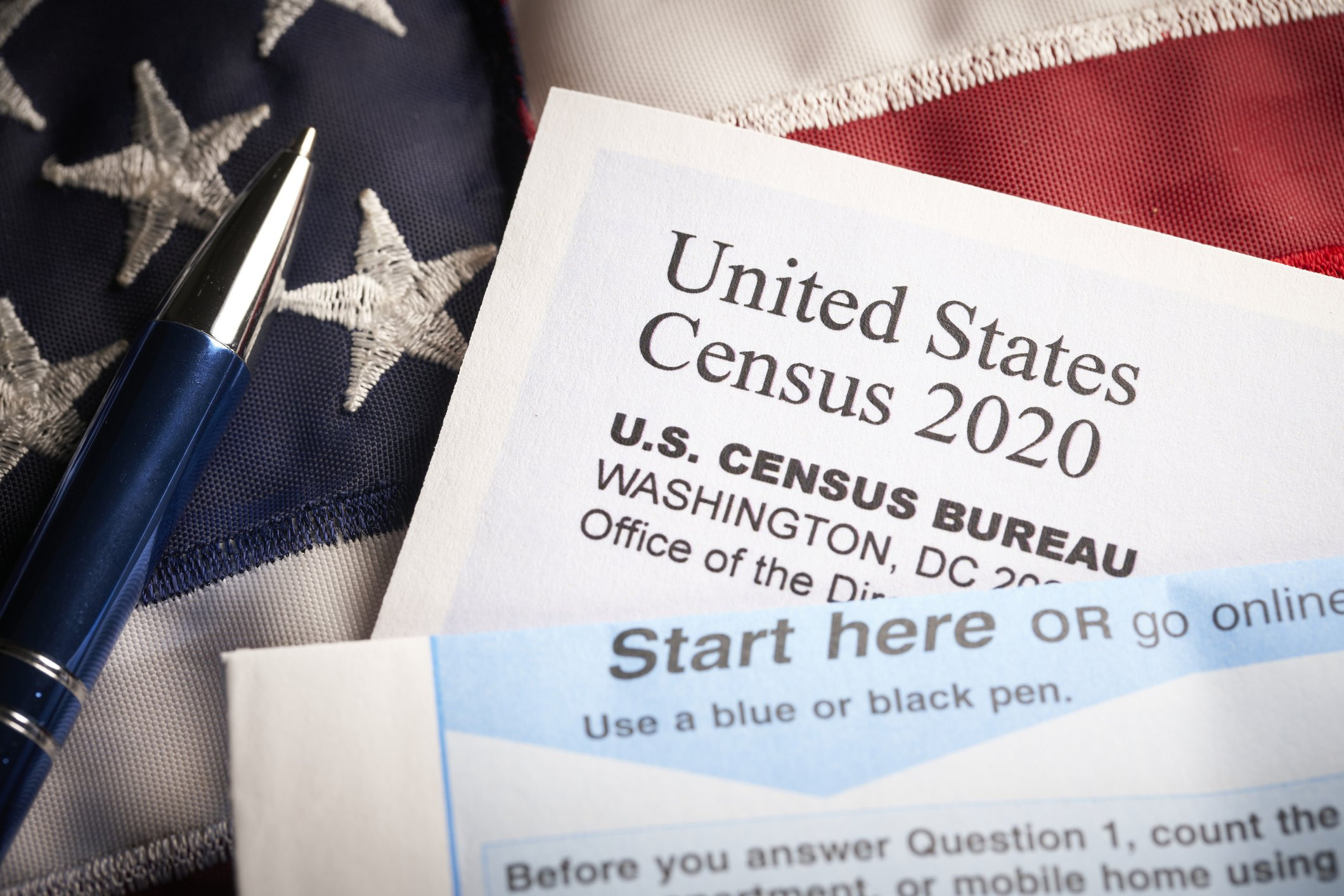 A copy of the United States Census 2020 form lays on an American flag with a blue pen to its left.