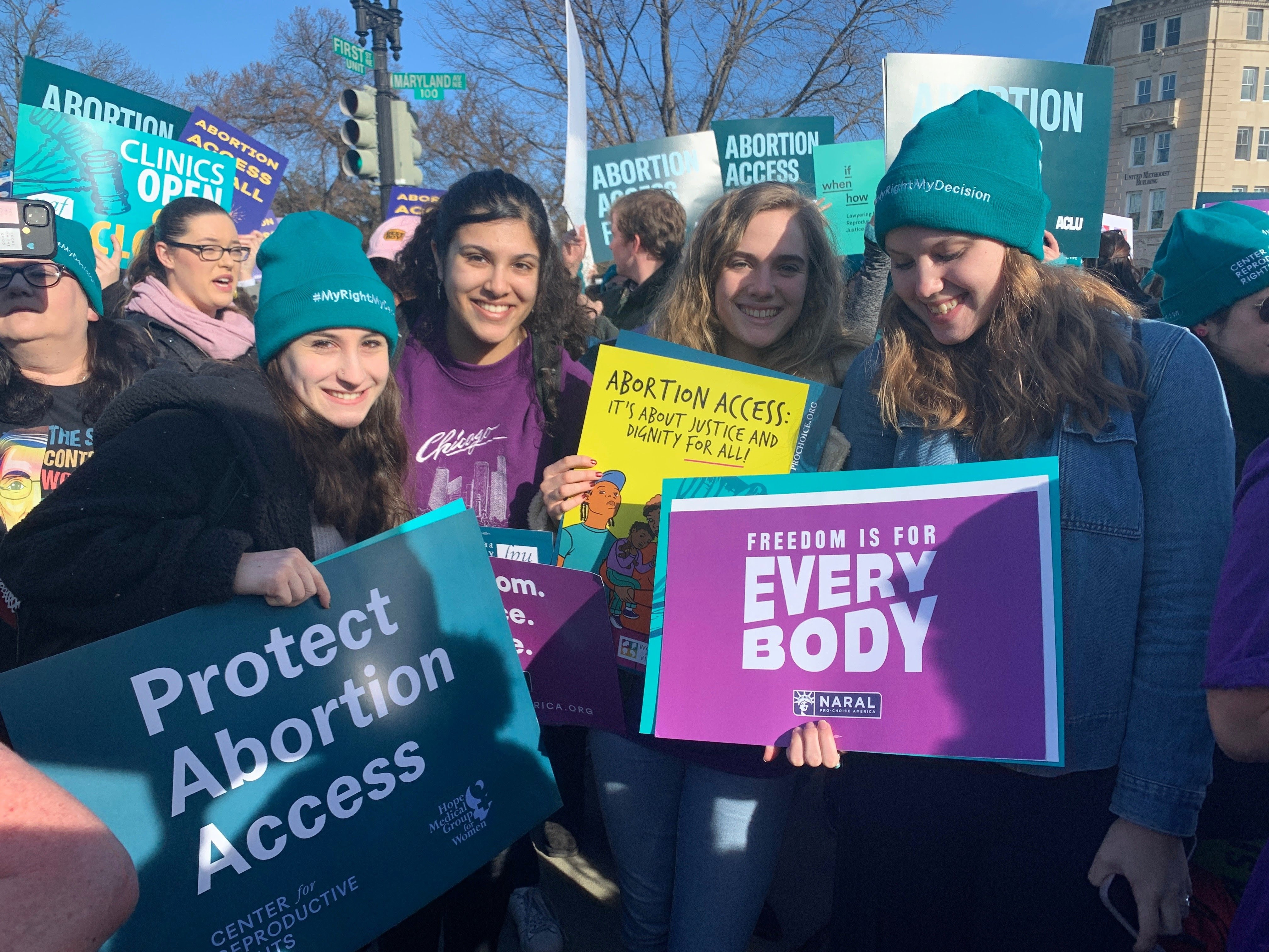 Four womxn posing with pro-abortion-access placards at a protest in front of the Supreme Court in Washington, DC.